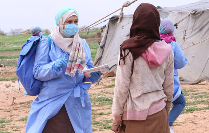 An outreach worker speaks to a Syrian woman about COVID-19.