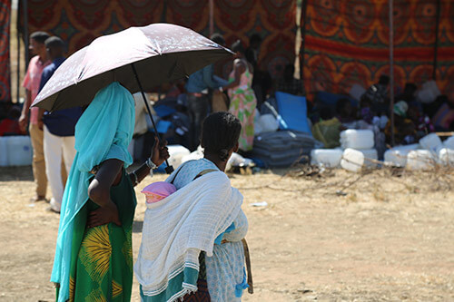 Two Ethiopian refugees huddle under an umbrella to escape the hot Sudanese sun.