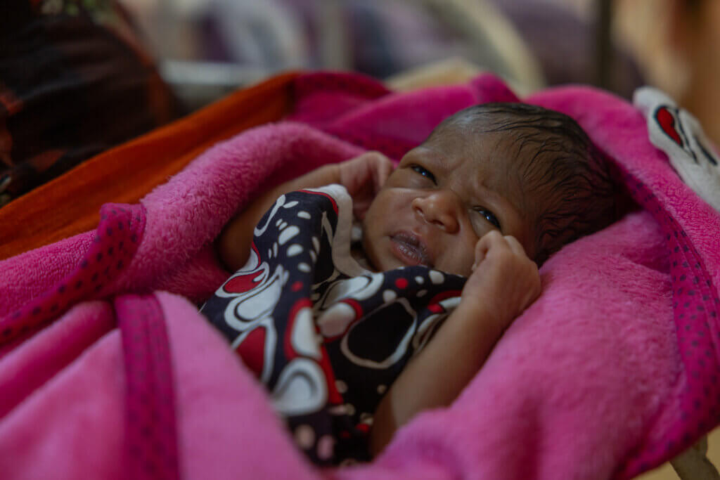 Baby swaddled in pink blanket looks at camera.