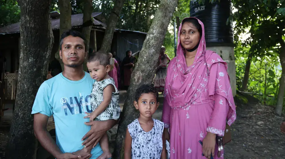 A woman stands with her husband and their two children outside their home in Bodipur village, Sunamganj. 