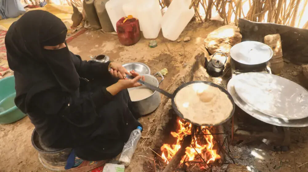 Displaced girl preparing bread over an open fire at a displacement site in Marib, Yemen